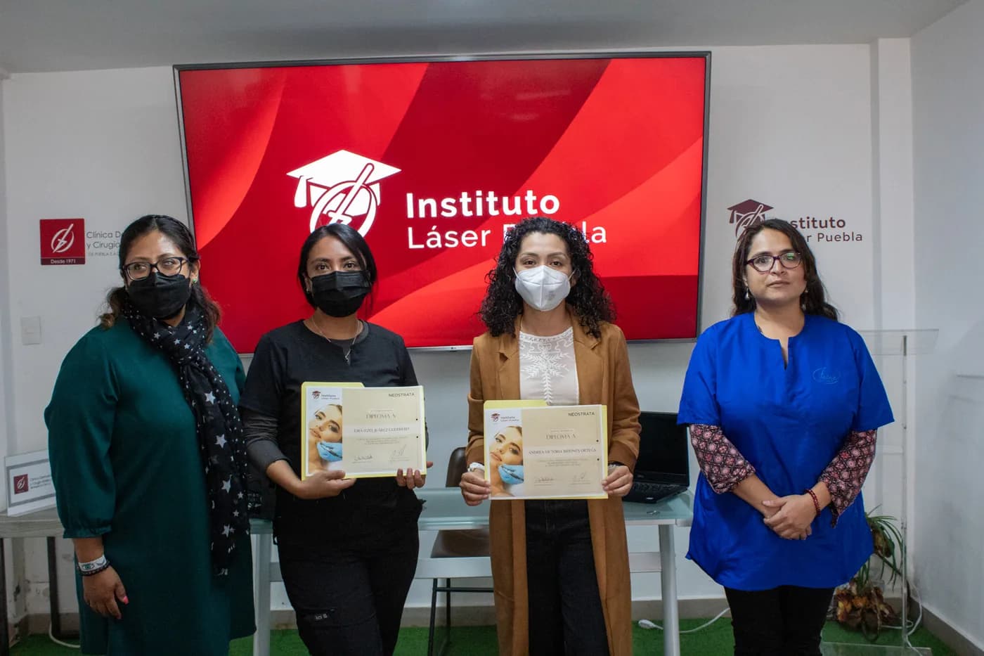 Egresadas del Diplomado sosteniendo su diploma frente a la pantalla del Instituto Láser Puebla